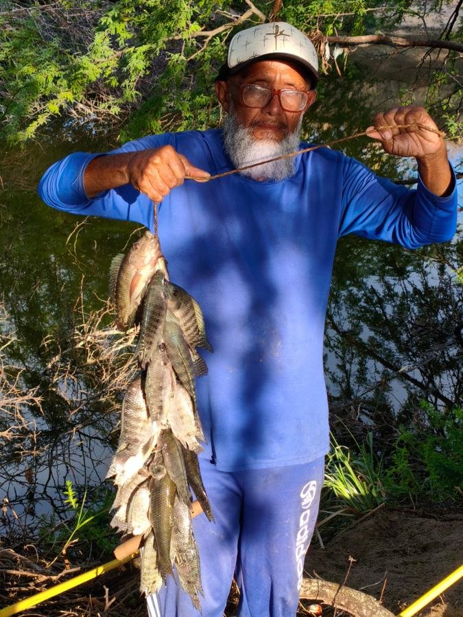 Pastor Lanzvaldo Ferreira segurando uma fieira de tilápias na beira do açude