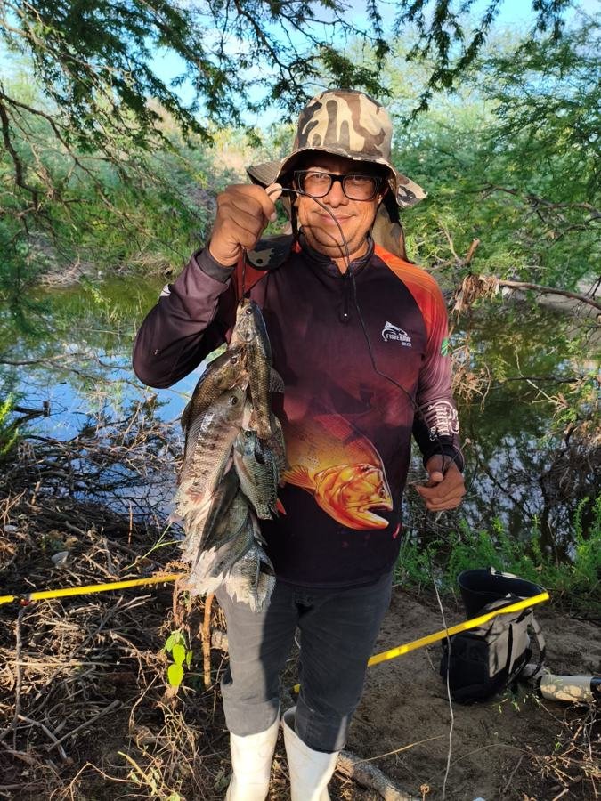 Pastor Maurício Oliveira segurando uma fieira de tilápias na beira do açude